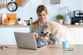 Beautiful lovely dog eating healthy breakfast of her smiling owner while she working with laptop in the kitchen at home Royalty Free Stock Photo