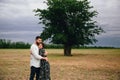 Beautiful loving couple resting in summer field on dry grass and big tree background