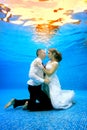 Beautiful loving couple in wedding dresses stands on her knees underwater at the bottom of the pool. Royalty Free Stock Photo