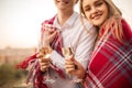Beautiful loving couple wrapped in one blanket holding glasses of champagne smiling at camera Royalty Free Stock Photo