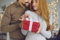 Beautiful loving young couple woman and man hugging and holding red holiday present box with gift Royalty Free Stock Photo