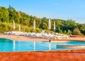 Beautiful luxury swimming pool with bright blue water, umbrellas and sunbeds in Tuscan landscape. Evening summer sunset Royalty Free Stock Photo