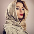 Beautiful makeup woman with red lipstick posing with head covered orient traditional shawl in studio. Toned closeup portrait