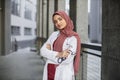 Beautiful Malay lady doctor wearing hijab, scrubs and white coat, outside modern clinic Royalty Free Stock Photo