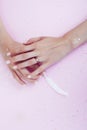 Beautiful manicured woman hands with white feather on pink background, wearing wedding ring