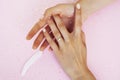 Beautiful manicured woman hands with white feather on pink background, wearing wedding ring