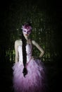 Beautiful masked woman with braided hairstyle in pink evening dress standing in a forest with her hand on her hip Royalty Free Stock Photo