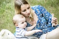 Beautiful mather and a baby boy sitting on grass and looking at electronic device