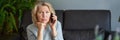 Beautiful mature blond woman talking on mobile phone at sofa. Royalty Free Stock Photo