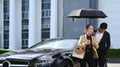 Beautiful mature businesswoman and her assistant standing by black car at parking with modern office building in Royalty Free Stock Photo