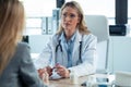 Beautiful mature female doctor talking while explaining medical treatment to patient in the consultation Royalty Free Stock Photo