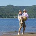 Beautiful mature man holding his beloved woman in his arms on a sandy beach on a summer sunny day against a background Royalty Free Stock Photo