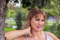 Beautiful mature middle-aged woman, 50 years old, blonde stands in the park against a background of greenery and grimaces in pain