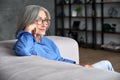 Beautiful mature older woman wearing glasses relaxing sitting on couch at home. Royalty Free Stock Photo