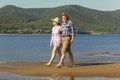 Beautiful mature sportive couple walks along the sandy river bank on a summer sunny day with mountains Royalty Free Stock Photo