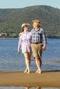 Beautiful mature sportive couple walks along the sandy river bank on a summer sunny day with mountains Royalty Free Stock Photo