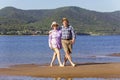 Beautiful mature sportive couple walks along the sandy river bank on a summer sunny day with mountains Royalty Free Stock Photo