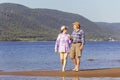 Beautiful mature sportive couple walks along the sandy river bank on a summer sunny day with mountains Royalty Free Stock Photo