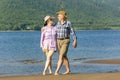 Beautiful mature sportive couple walks along the sandy river bank on a summer sunny day with mountains Royalty Free Stock Photo