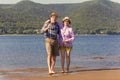 mature sportive couple walks along the sandy river bank on a summer sunny day with mountains in the background Royalty Free Stock Photo