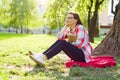 Beautiful mature woman with glasses reading book sitting on the grass near the tree in the park at sunset Royalty Free Stock Photo