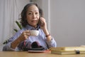 Beautiful mature woman holding coffee cup and talking on mobile phone while sitting in living room Royalty Free Stock Photo