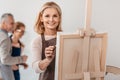 beautiful mature woman smiling at camera while painting on easel at art Royalty Free Stock Photo