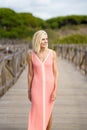 Beautiful mature woman walking along a wooden path near the beach., wearing a nice orange dress. Royalty Free Stock Photo