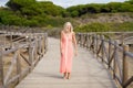 Beautiful mature woman walking along a wooden path near the beach., wearing a nice orange dress. Royalty Free Stock Photo