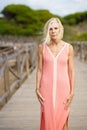 Beautiful mature woman walking along a wooden path near the beach., wearing a nice orange dress. Royalty Free Stock Photo