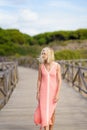 Beautiful mature woman walking along a wooden path near the beach., wearing a nice orange dress. Royalty Free Stock Photo