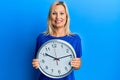Beautiful middle age blonde woman holding big clock smiling with a happy and cool smile on face Royalty Free Stock Photo