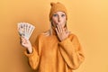 Beautiful middle age blonde woman holding 10 united kingdom pounds banknotes covering mouth with hand, shocked and afraid for