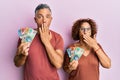 Beautiful middle age couple holding australian dollars covering mouth with hand, shocked and afraid for mistake