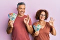 Beautiful middle age couple holding australian dollars doing ok sign with fingers, smiling friendly gesturing excellent symbol