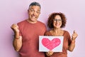 Beautiful middle age couple holding heart draw screaming proud, celebrating victory and success very excited with raised arm Royalty Free Stock Photo