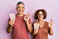 Beautiful middle age couple holding 10 united kingdom pounds banknotes doing ok sign with fingers, smiling friendly gesturing