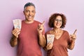 Beautiful middle age couple holding 10 united kingdom pounds banknotes smiling happy pointing with hand and finger to the side