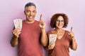 Beautiful middle age couple holding 10 united kingdom pounds banknotes smiling with an idea or question pointing finger with happy