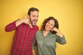 Beautiful middle age couple over isolated yellow background smiling doing phone gesture with hand and fingers like talking on the Royalty Free Stock Photo