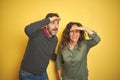 Beautiful middle age couple over isolated yellow background very happy and smiling looking far away with hand over head Royalty Free Stock Photo