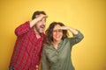 Beautiful middle age couple over isolated yellow background very happy and smiling looking far away with hand over head Royalty Free Stock Photo