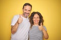 Beautiful middle age couple together standing over isolated yellow background happy with big smile doing ok sign, thumb up with Royalty Free Stock Photo