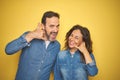 Beautiful middle age couple together standing over isolated yellow background smiling doing phone gesture with hand and fingers Royalty Free Stock Photo