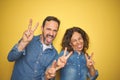 Beautiful middle age couple together standing over isolated yellow background smiling with tongue out showing fingers of both Royalty Free Stock Photo