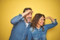 Beautiful middle age couple together standing over isolated yellow background very happy and smiling looking far away with hand Royalty Free Stock Photo