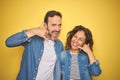 Beautiful middle age couple together wearing denim shirt over isolated yellow background smiling doing phone gesture with hand and Royalty Free Stock Photo