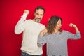 Beautiful middle age couple wearing winter sweater over isolated red background showing arms muscles smiling proud Royalty Free Stock Photo