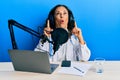 Beautiful middle age doctor woman working at radio studio amazed and surprised looking up and pointing with fingers and raised Royalty Free Stock Photo