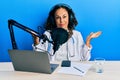 Beautiful middle age doctor woman working at radio studio clueless and confused expression with arms and hands raised Royalty Free Stock Photo